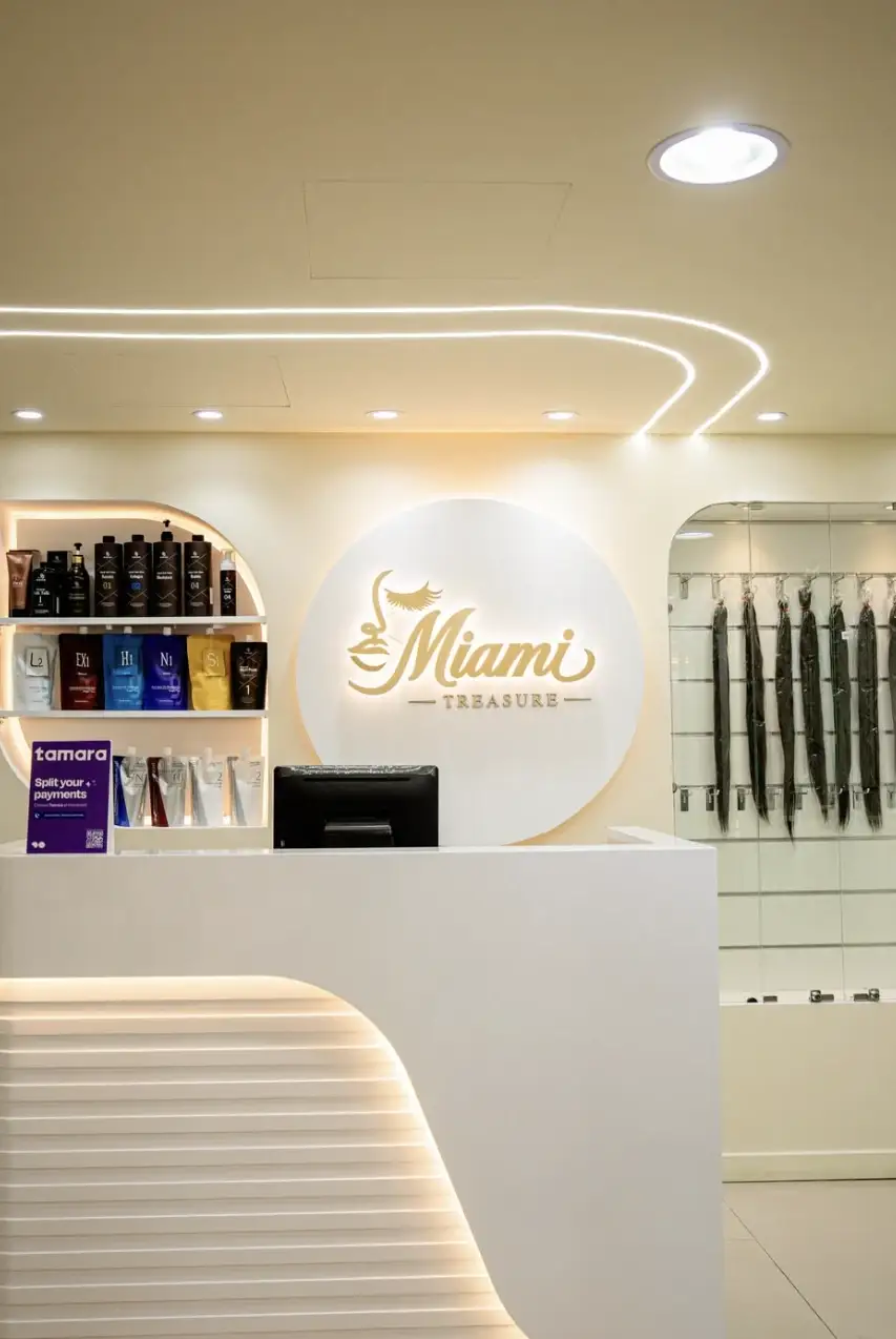 The white curved reception desk with the gold-lit logo disc behind it, product shelves on the left and a wall of hair extensions on the right